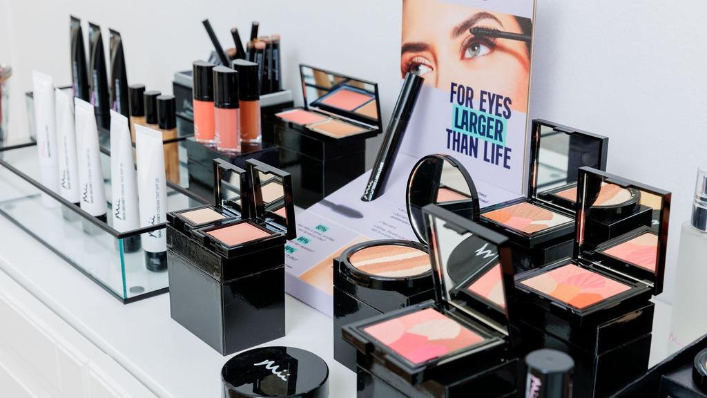 Et udvalg af makeupprodukter, herunder foundation, blush og øjenskygge, præsenteret på et bord.