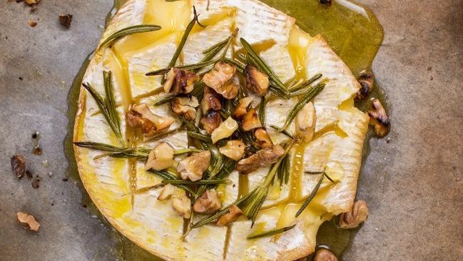 Bagt brie med rosmarin og hakkede valnødder på en bageplade, dryppet med olivenolie.