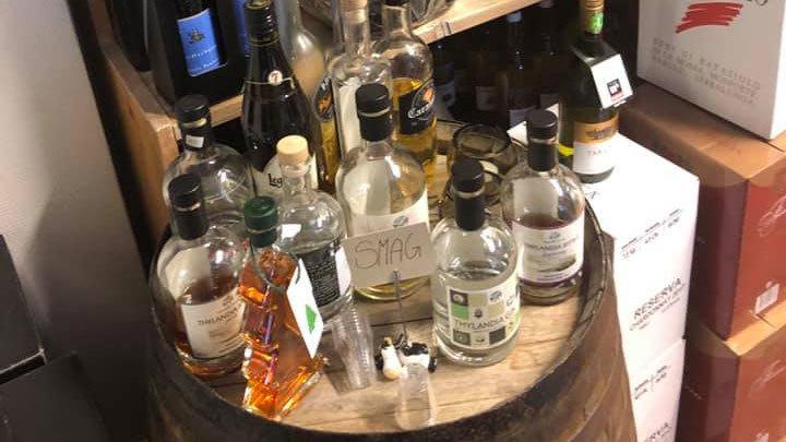 En træfad med forskellige flasker spiritus, herunder whisky og rom, i en vinkælder.