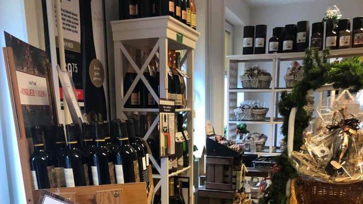 Inde i en vinbutik med hylder fyldt med rødvine, delikatesser og gaveartikler.