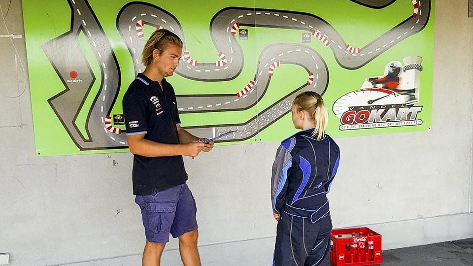 En instruktør forklarer en ung kører om gokartbanen på en vægplakat.