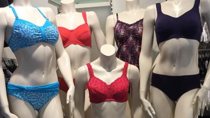 Fem mannequinfigurer iført forskellige bh'er og trusser i blå, rød og lilla farver i en butik.