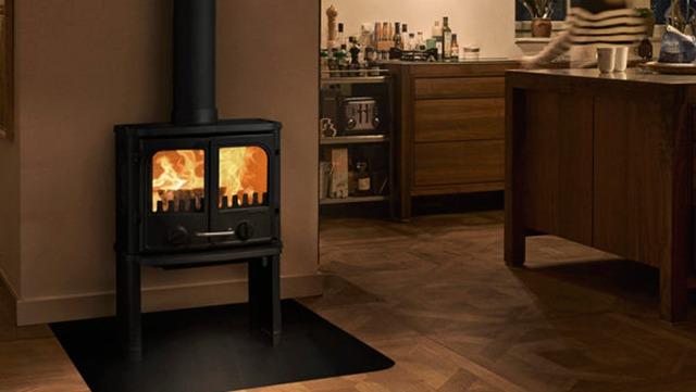 En sort brændeovn med flammer, placeret i et moderne køkken med træmøbler og en varm atmosfære.
