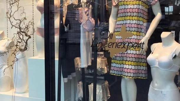 Vinduesudstilling med mannequiner iført farverigt tøj og undertøj i en butik.