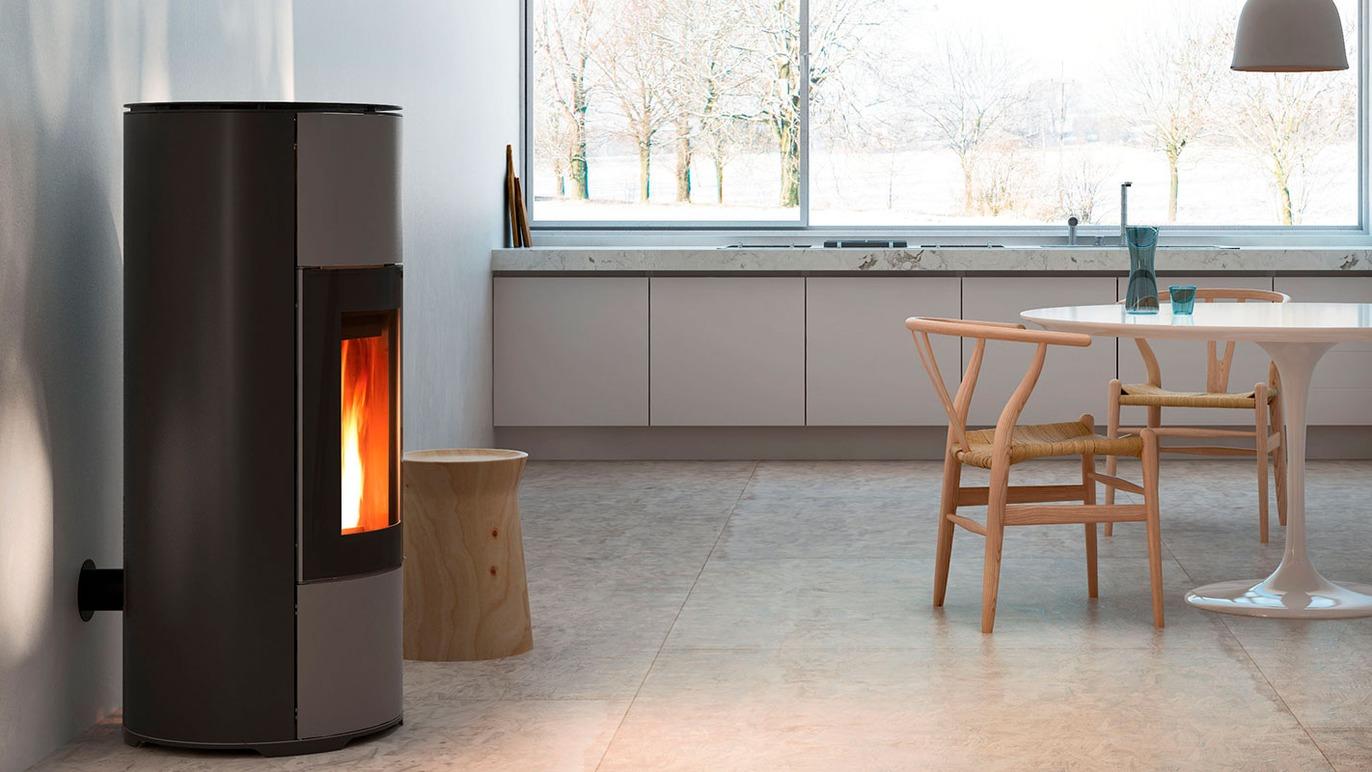 Moderne brændeovn i stue med store vinduer og minimalistisk køkkenindretning.