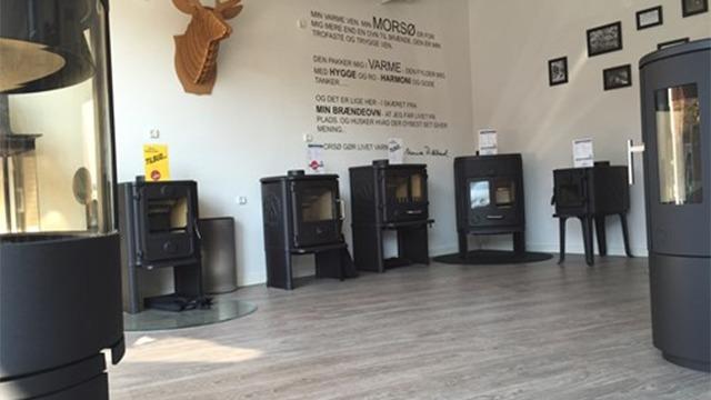 Visning af en moderne pejseshowroom med flere sorte pejse og en væg med information og billeder.