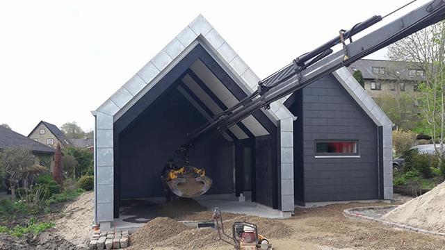 Nybygget hus med skråtag og en kran, der leverer materialer til konstruktionen.