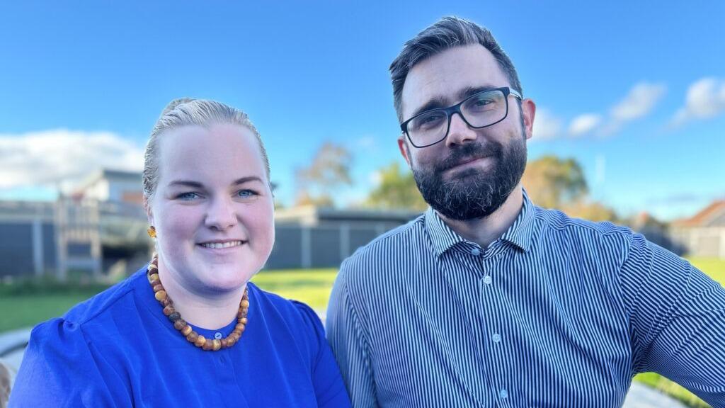 To personer smiler til kameraet i en solrig have med blå himmel i baggrunden.