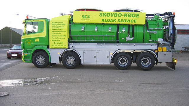 Grøn kloakservice lastbil med gul tekst og logo, parkeret på en asfaltvej.