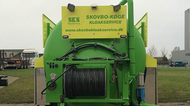 Grøn kloakservicevogn med logo og webadresse, parkeret på en græsplæne.