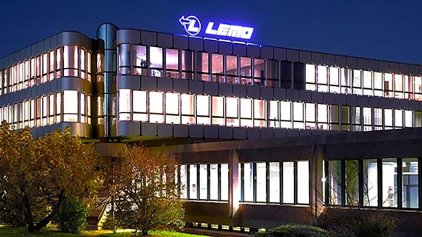 Moderne kontorbygning med LEMO-logo oplyst om natten, omgivet af træer og en klar himmel.