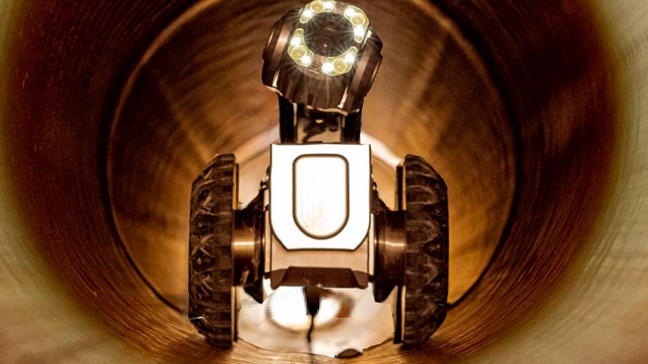 En robot med lys, der kører ind i et rør, med metaloverflade og gummihjul.