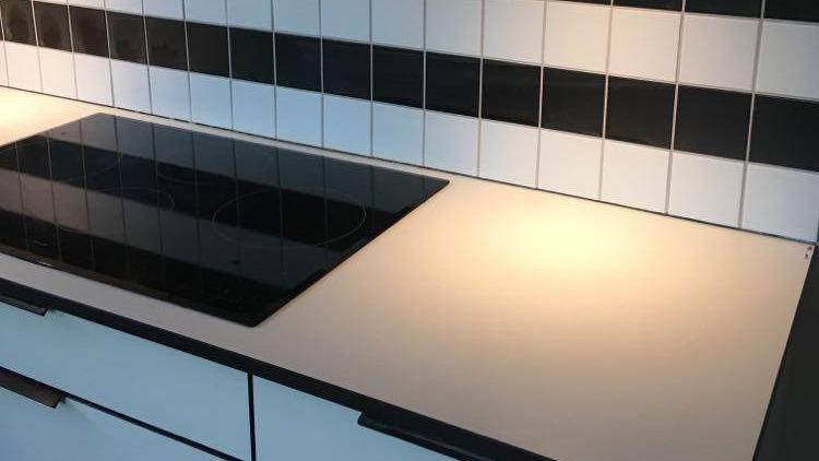 Moderne køkkenbordplade med induktionskogeplade og sort-hvide fliser på væggen.