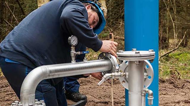 En tekniker arbejder med en metalrørledning og en trykmåler i en skov.