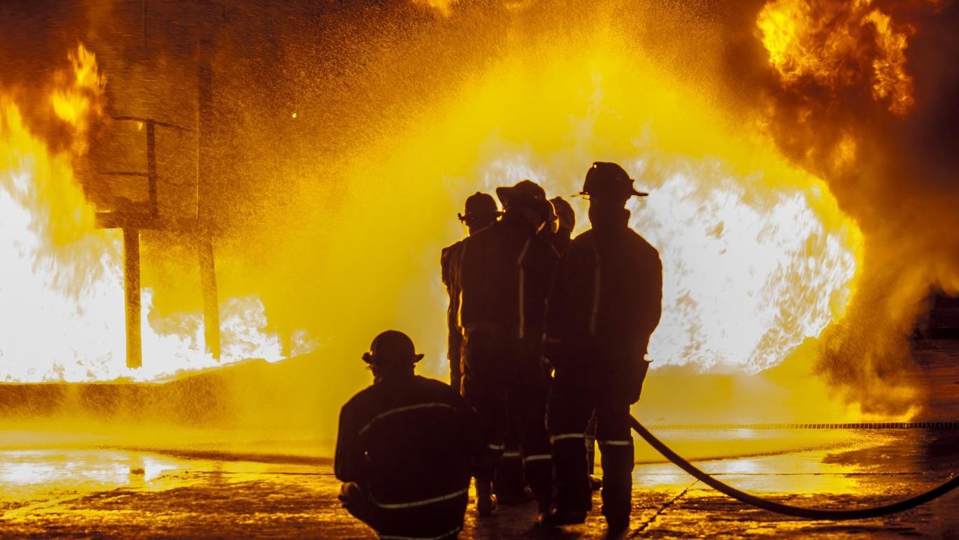 Brandfolk står foran en stor flamme, mens de forbereder sig på at slukke ilden med en brandslange.