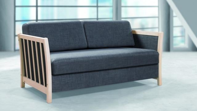 Sofa med mørkeblå betræk og træramme, placeret i et lyst rum med store vinduer.