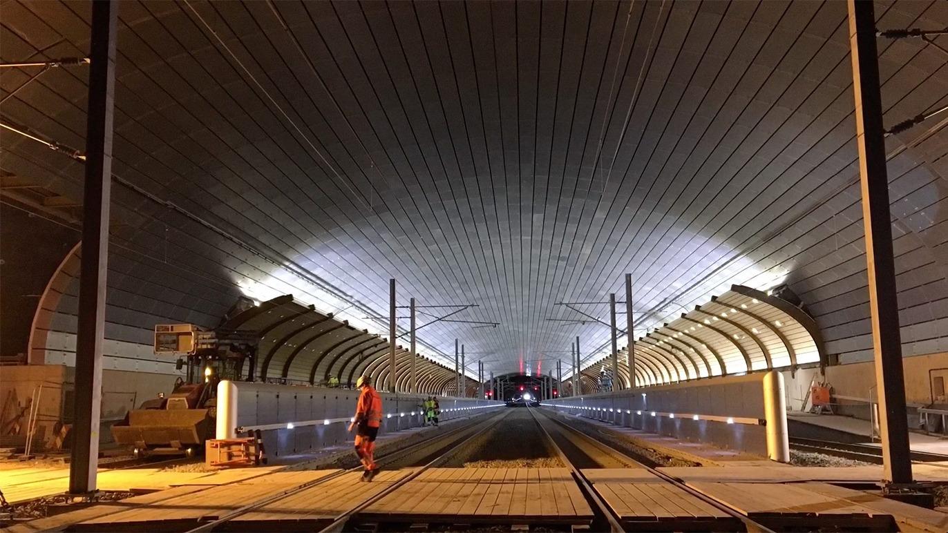 En arbejder står på skinnerne i en tunnel med moderne belysning og buet metalloft.