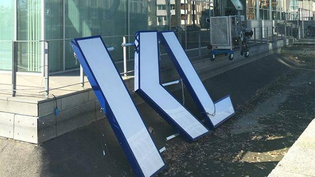 To store skilte står på fortovet ved en bygning, med blå rammer og hvide flader.