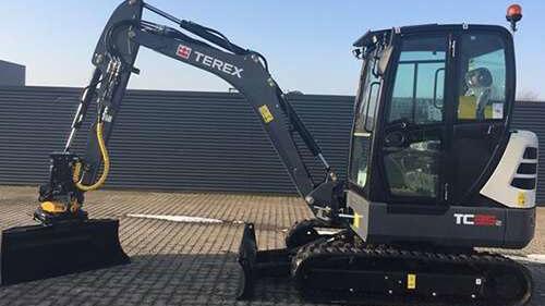 En Terex minigraver med skovl, parkeret på en flisebelagt overflade.