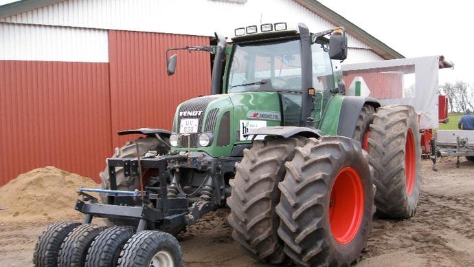 En grøn traktor med store dæk står foran en lade på en gård.