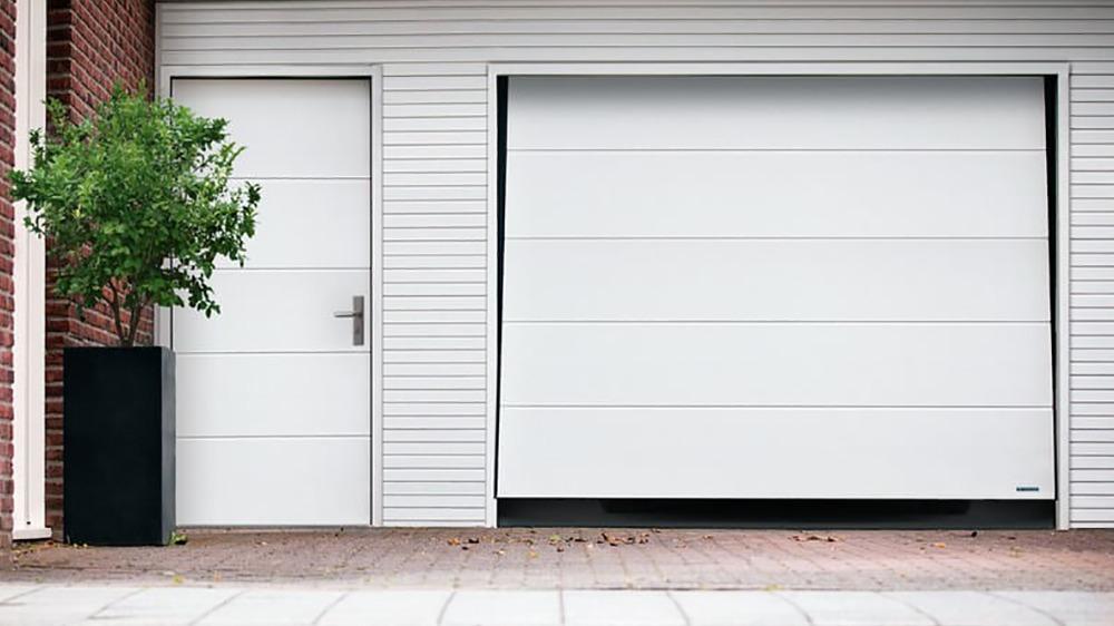 Hvid garageport og dør ved en moderne bygning med en lille plante i en krukke.