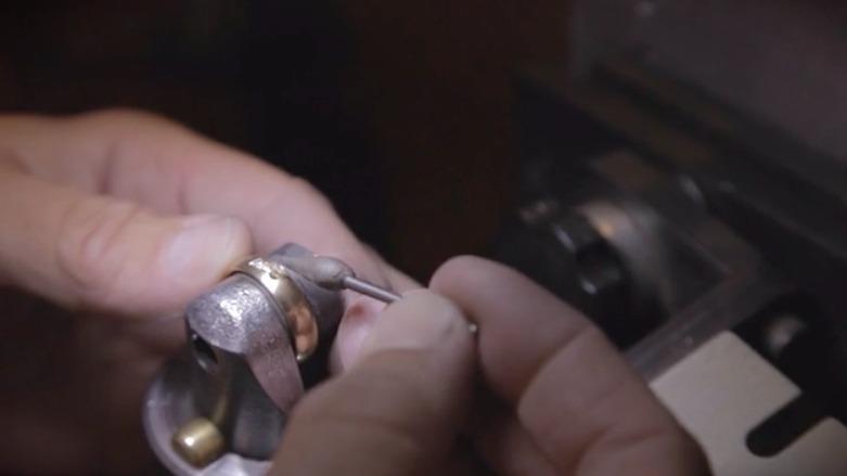 Hånd, der arbejder med en metalgenstand på en maskine, der viser præcisionsarbejde i håndværk.