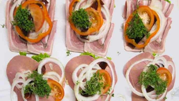 Lækre smørrebrød med skinke, tomat, løg, peberfrugt og friske krydderurter på en hvid tallerken.