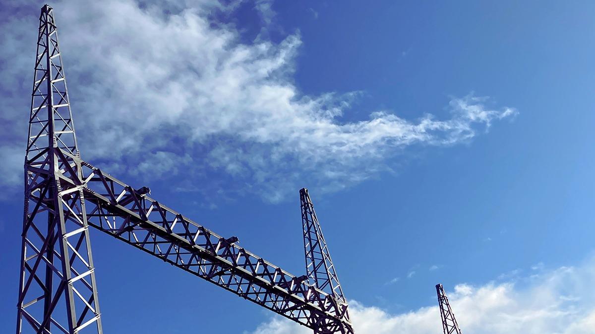 Høj metalstruktur med antenner mod en blå himmel med skyer.