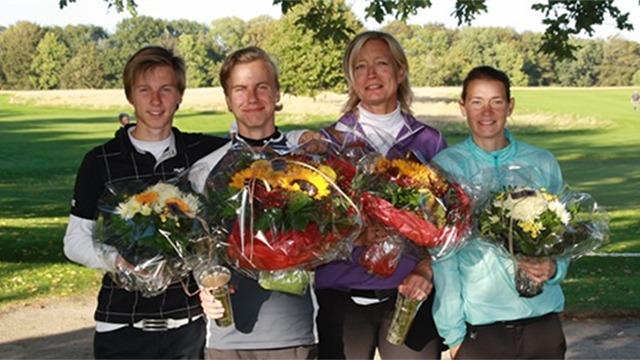 Fire glade personer står sammen med store blomsterbuketter på en golfbane i solskin.
