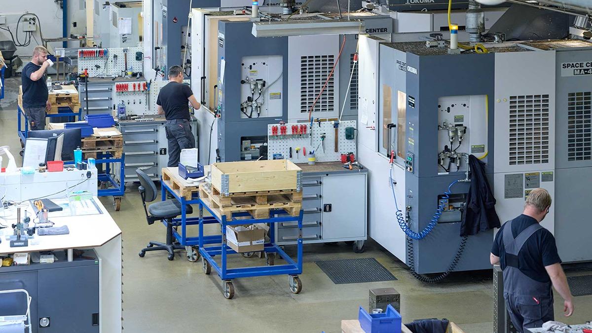 Billede af en moderne fabrik med arbejdere, maskiner og arbejdsstationer i et produktionsmiljø.