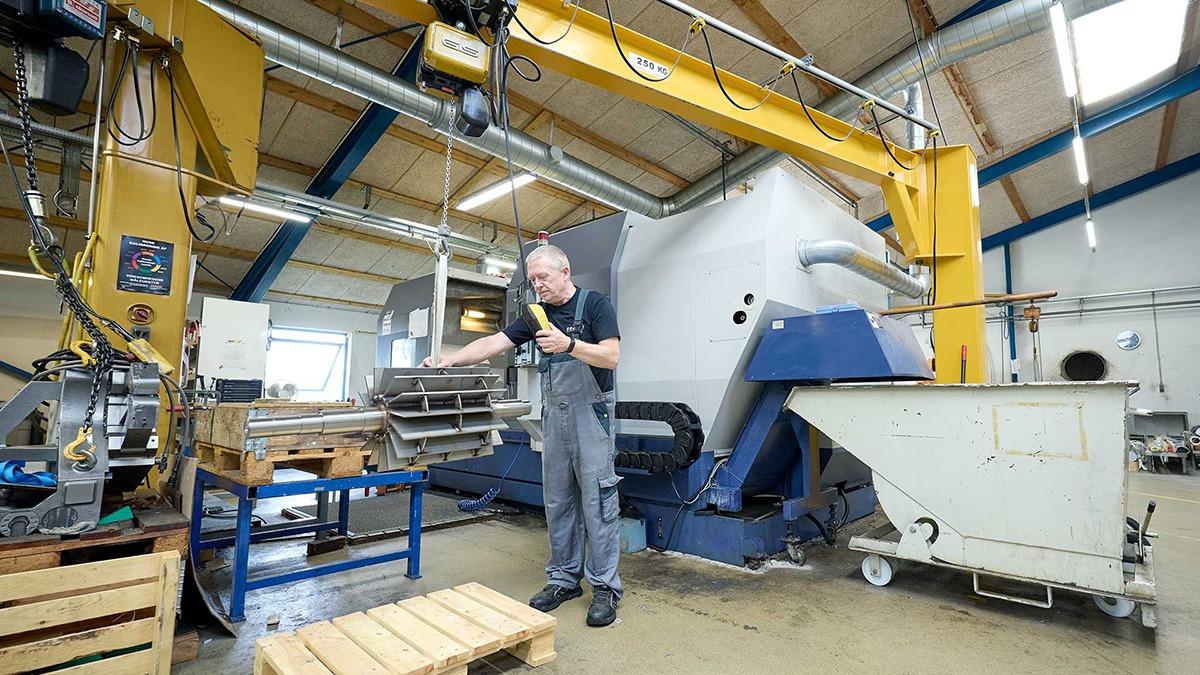 En mand arbejder ved en stor maskine i en fabrik, omgivet af metalplader og udstyr.