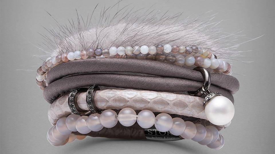 Et sæt elegante armbånd i grå og lyserøde nuancer med perler og bløde tekstiler.