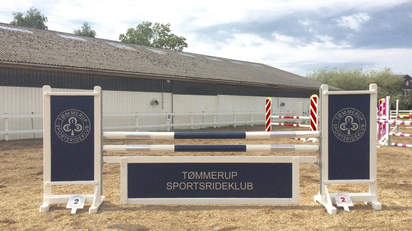Springbane med forhindringer og banner fra Tømmerup Sportsrideklub i en ridesportshal.