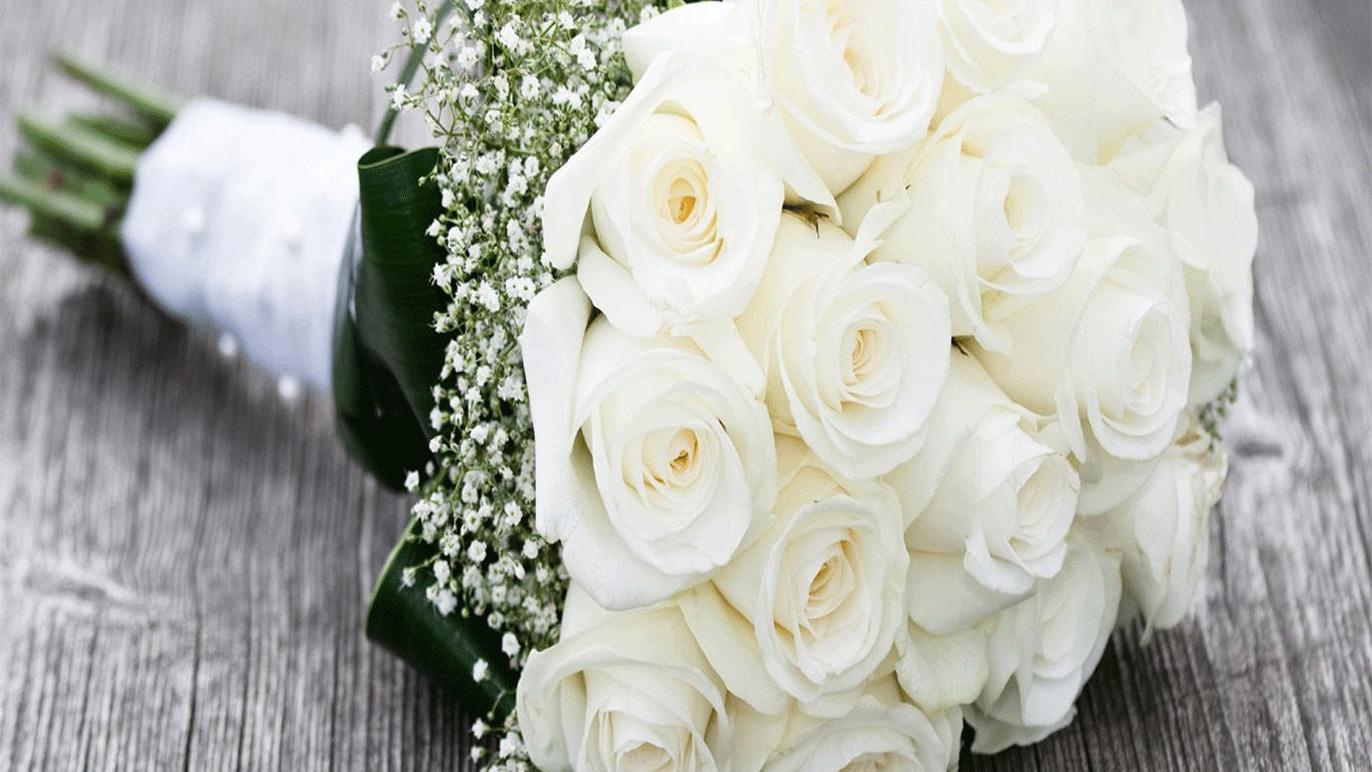 En smuk buket med hvide roser og gypsophila, bundet med et bånd på en træoverflade.