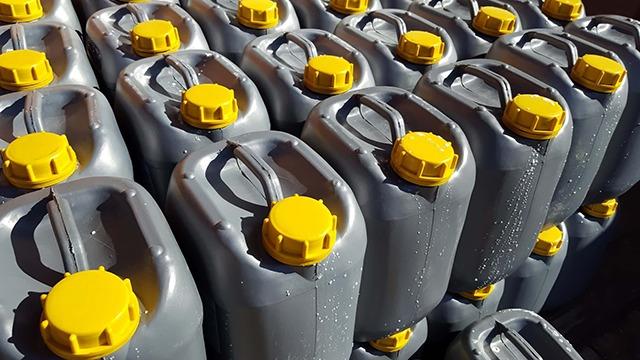 Grå plastbeholdere med gule låg stablet i rækker, fyldt med væske.