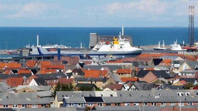 Udsigt over en havn med færger og farverige tage på bygninger i forgrunden.
