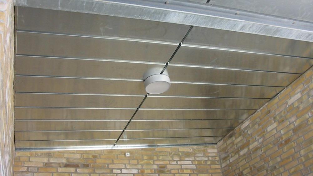 Et metalloft med synlige stålplader og en rund loftlampe i et rum med murstensvægge.