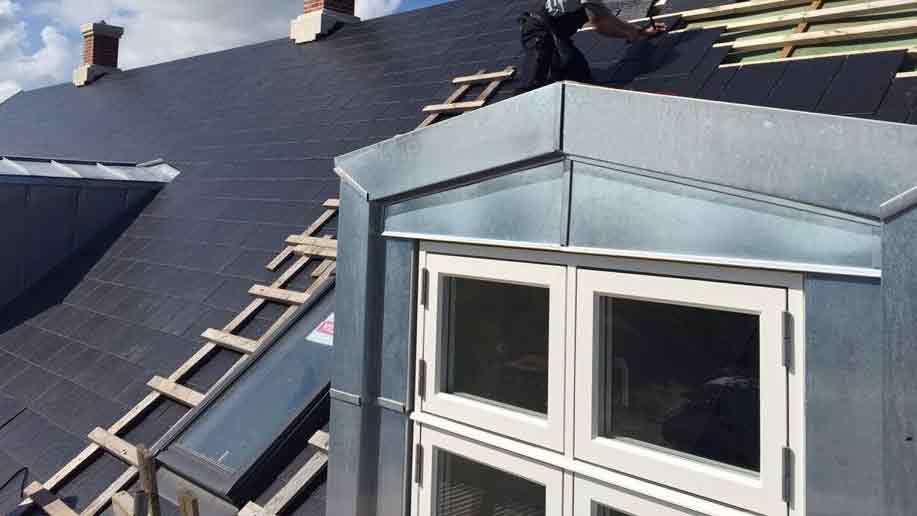 Tagdækker arbejder på et hus med grå tagsten og en moderne vinduesramme.