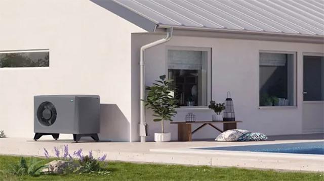 En moderne varmepumpe ved siden af et hus med en swimmingpool og grøn græsplæne.