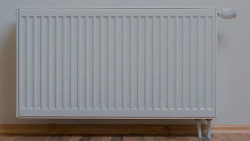 Hvid radiator med ribbet overflade monteret på væggen i et rum med trægulv.