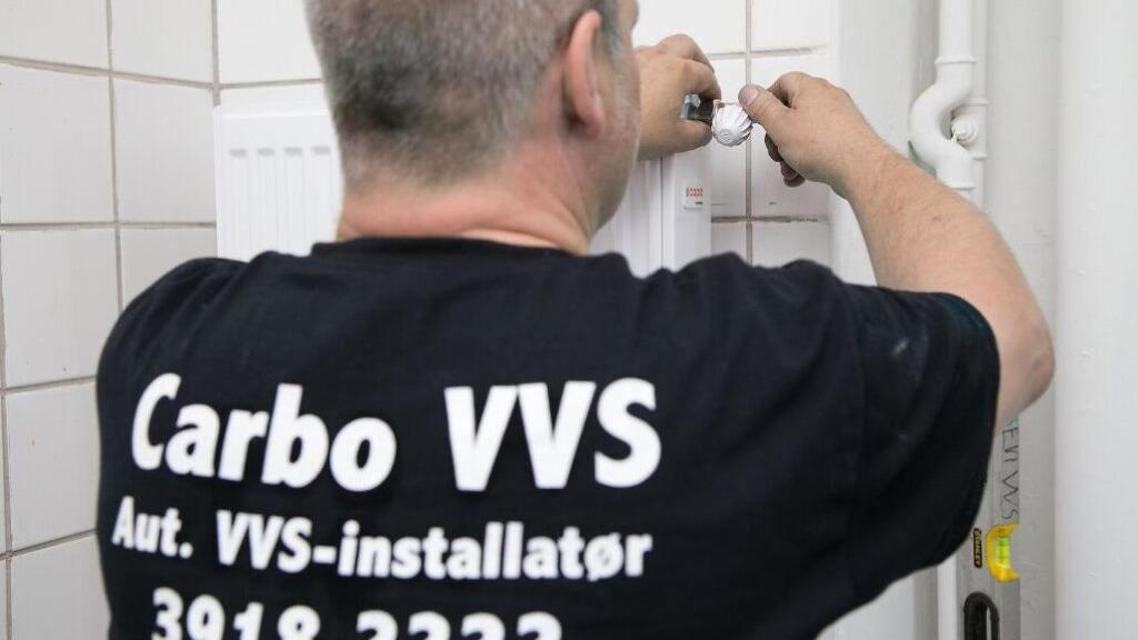 En VVS-installatør arbejder på en radiator med værktøj, iført en T-shirt med teksten "Carbo VVS".