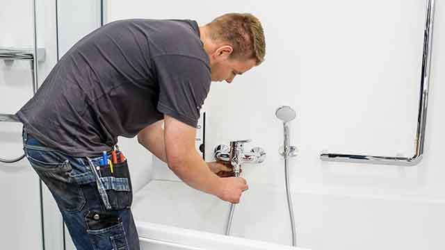 En håndværker, der arbejder på en badekarinstallation, mens han justerer vandhanen.