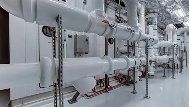 Rørinstallation i et moderne teknisk rum med hvide rør og metalstøtter.