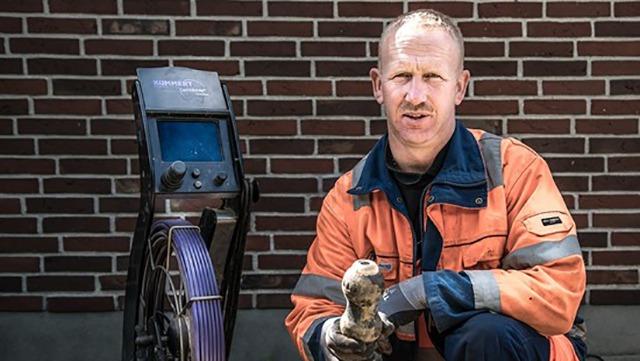 En mand i arbejdstøj sidder ved en maskine med en kabelrulle og holder en værktøj i hånden.