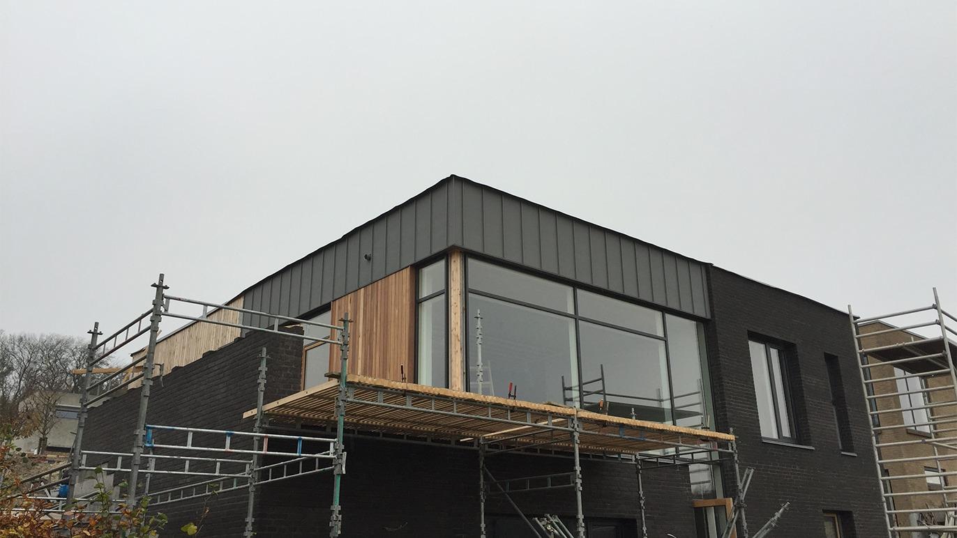 Moderne hus under opførelse med store vinduer og trædetaljer, omgivet af stilladser.