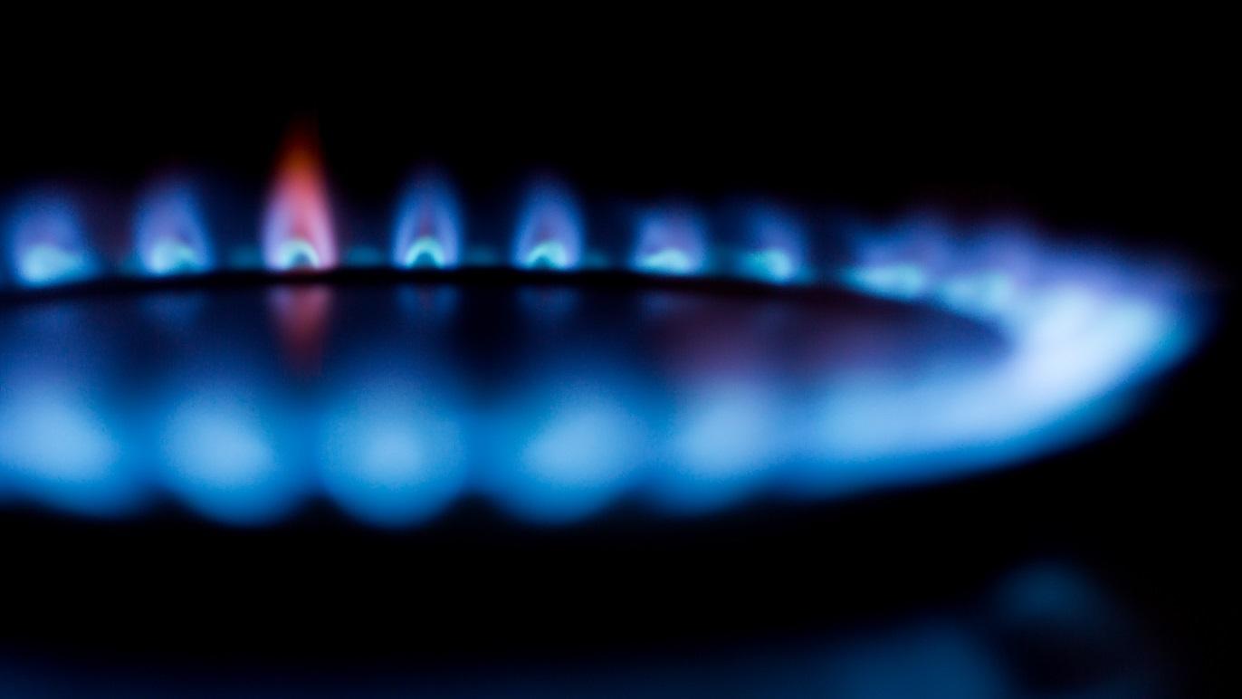 Blå gasflamme på en gaskomfur, der lyser op i mørket med en rødlig spids.