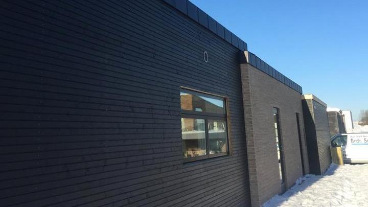 En bygning med mørke vægge og et vindue, beliggende i et snedækket område under en klar blå himmel.