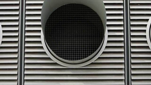 Ventilationssystem med runde gitteråbninger på en bygning med lodrette lameller.