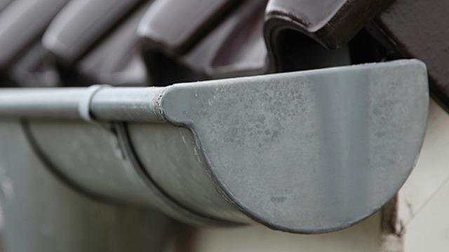 Nærbillede af en grå tagrende på et hus med mørke tagsten.