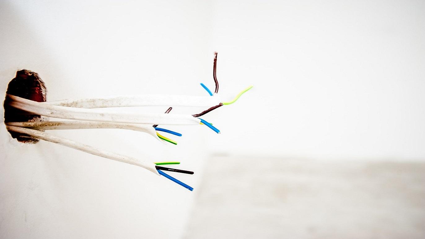 Elektriske ledninger stikker ud fra en væg i et tomt rum med hvidt malede vægge.